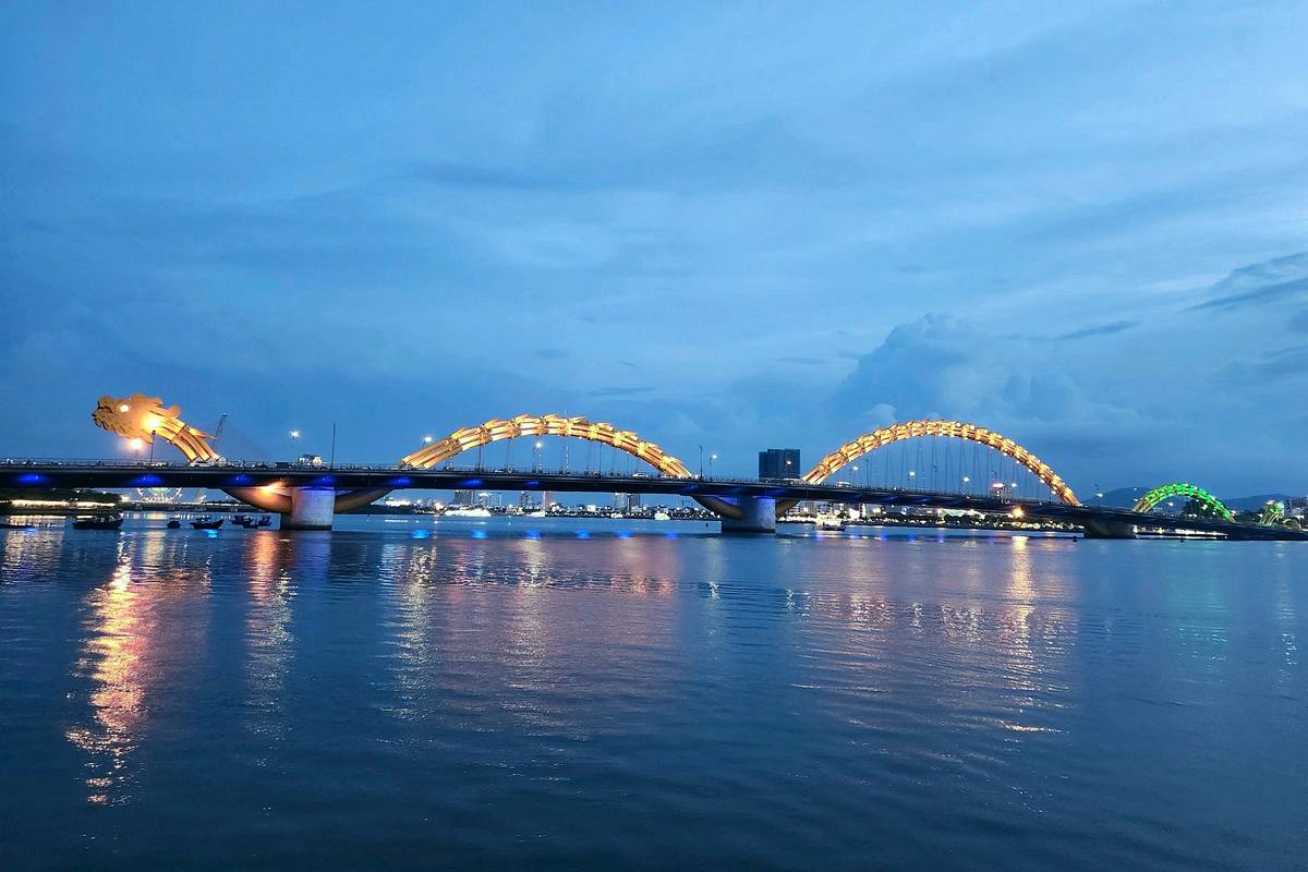 The Dragon Bridge in Da Nang lit up in gold and reflected in the Han River at dusk