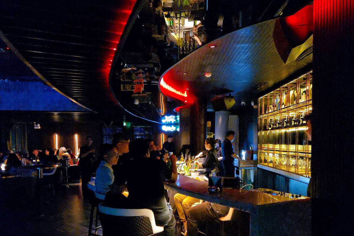 Guests at a stylish dimly lit bar in Ho Chi Minh City with shelves of bottles behind