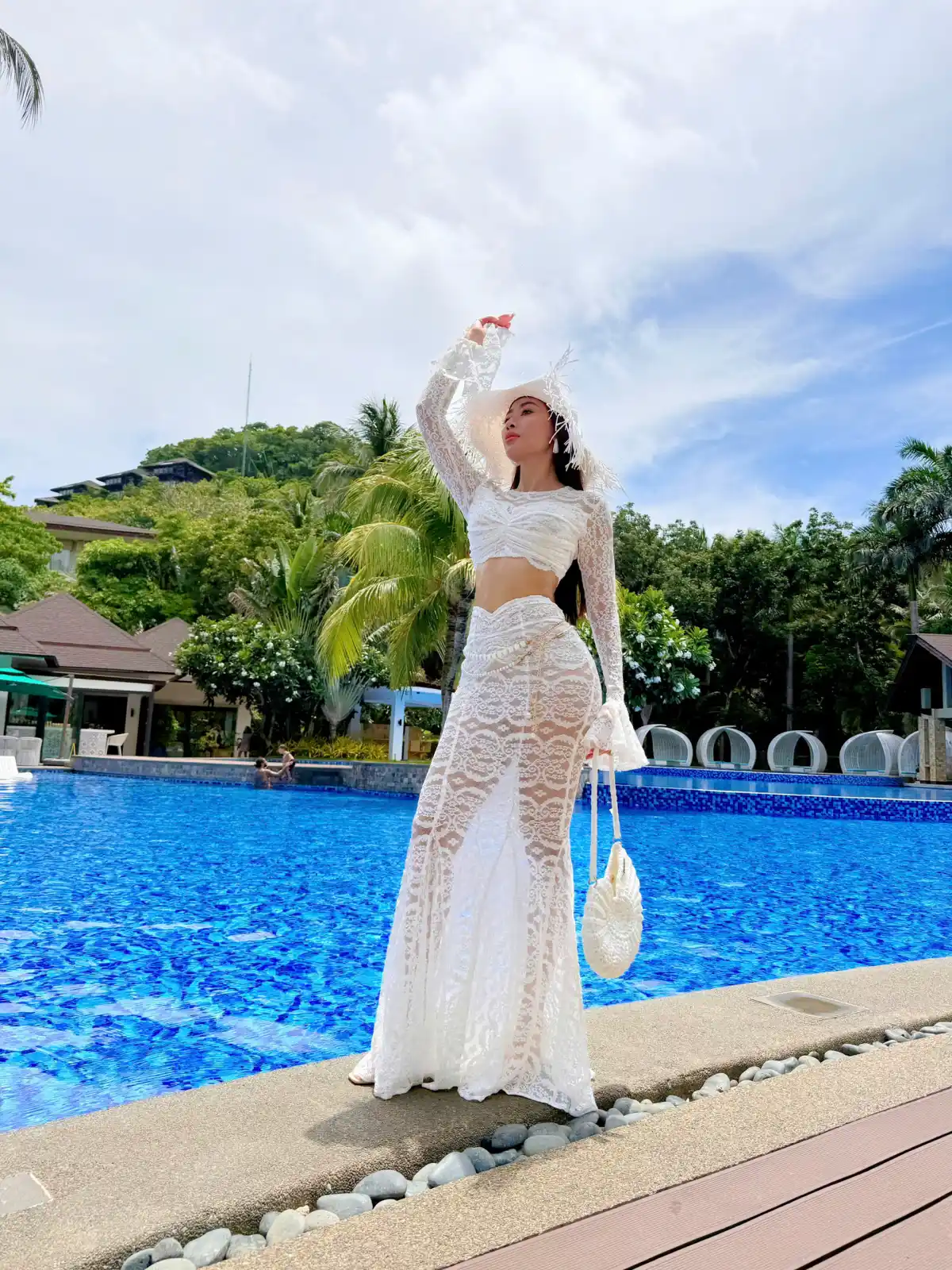 Khách mặc váy ren trắng đứng bên hồ bơi lớn của resort