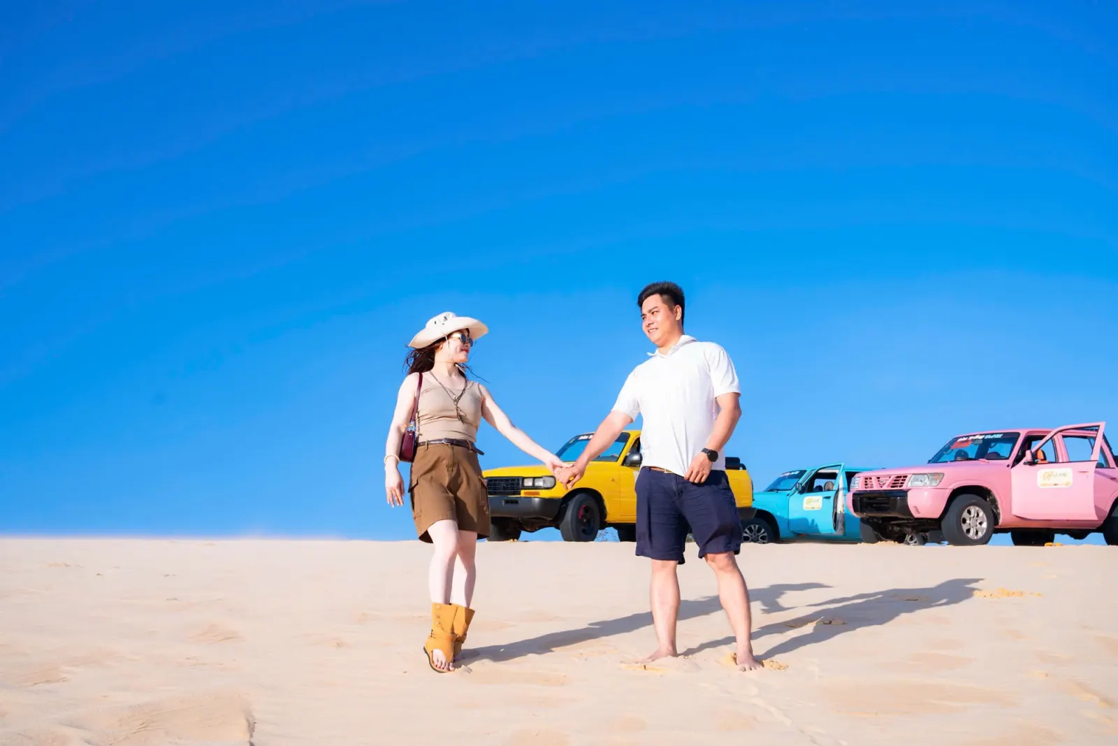 Khách đoàn công ty đi trên đồi cát, sau lưng là xe jeep nhiều màu